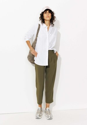Chemise blanche à boutons, pantalon vert olive, baskets argentées et sac à imprimé léopard. Cheveux bouclés et casquette rose pâle complètent le look.