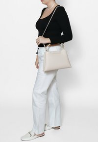 Beige leren handtas met een gestructureerd ontwerp, een bovenhandvat en een afneembare schouderband, met minimale hardware en een gladde textuur.