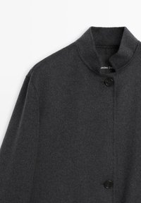 Cappotto di lana grigio scuro con colletto alto, chiusura a singolo bottone nero e una texture liscia. Design minimalista senza motivi visibili.
