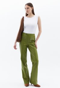 Zelené vysoké flared kalhoty s dvěma zipovými předními kapsami, kombinované s těsným bílým topem bez rukávů a hnědou kabelkou.