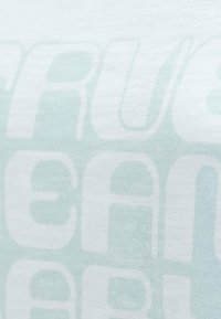 T-shirt vert menthe clair avec une texture douce, ornée d'un grand texte graphique blanc. Le design a un aspect légèrement usé.