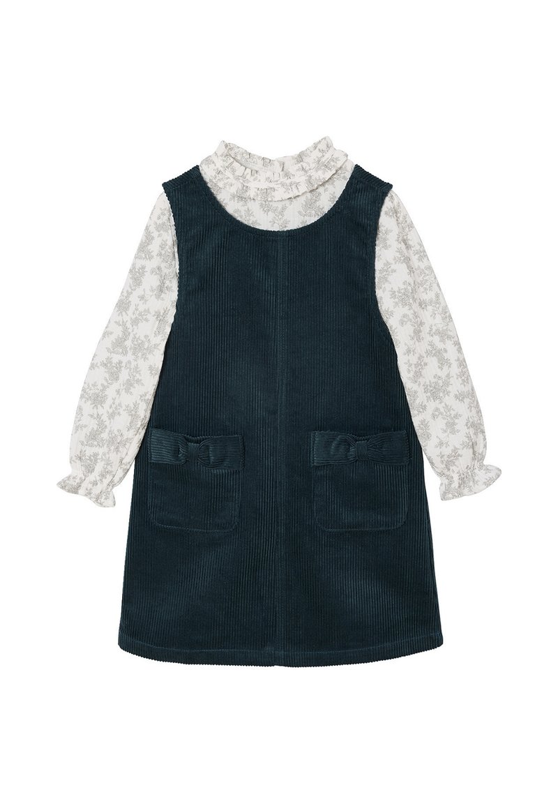 Dunkelgrünes Cordkleid mit Rüschenausschnitt und langen Ärmeln. Weiße Bluse mit leichtem Blumenmuster und zwei frontalen Taschen.