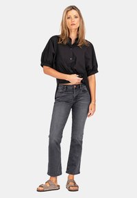 Schwarz, kurzärmliges Hemd mit Knopfleiste und abgerundetem Saum, kombiniert mit dunkelgrauen Slim-Fit-Jeans und grauen Sandalen mit zwei Riemen.