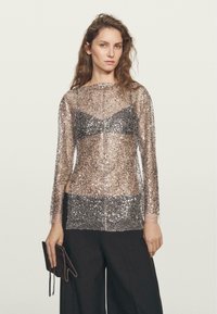Top trasparente a maniche lunghe con paillettes argentate e nere sparse, con un design di bralette nera solida sotto. Accompagnato da una pochette scura.