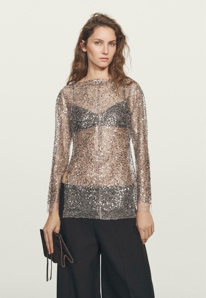 Top trasparente a maniche lunghe con paillettes argentate e nere sparse, con un design di bralette nera solida sotto. Accompagnato da una pochette scura.