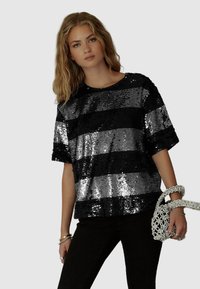 Top a strisce nere e argentate in paillettes con una vestibilità ampia e maniche corte, abbinato a pantaloni neri e una borsa a tracolla intrecciata argentata.