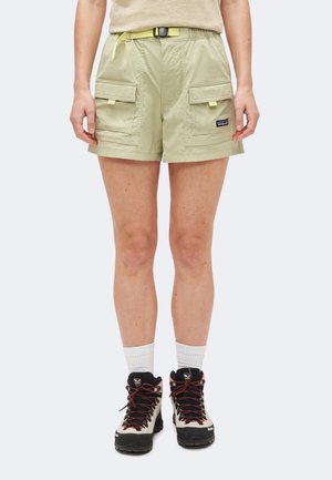 Personne portant un short cargo beige avec des poches à rabat à l’avant, des chaussettes blanches et des chaussures de randonnée beiges et noires avec des lacets rouges.