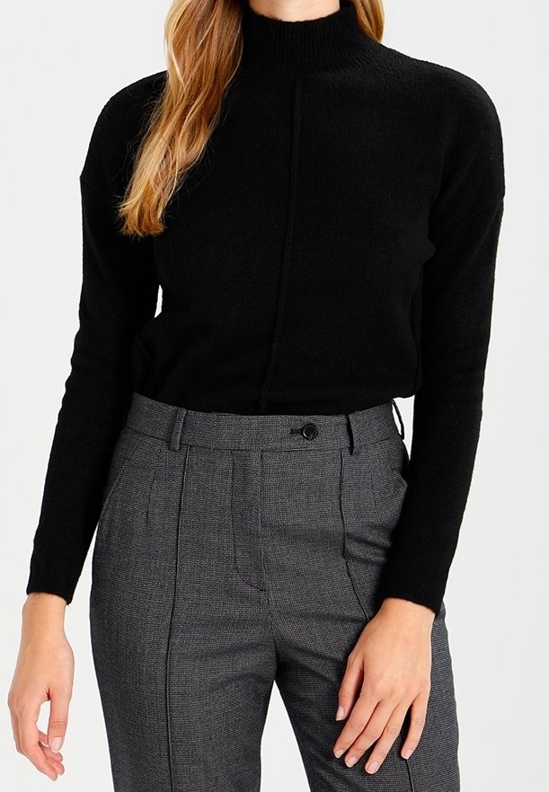 Schwarzer Strick-Turtleneck-Pullover mit strukturiertem Rippmuster, versehen mit einer Naht vorne, kombiniert mit grauen karierten Hochbundhosen.