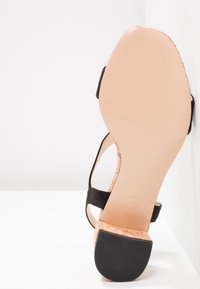 Sandale à semelle beige avec sangle noire et talon bloc à texture liège, vue de la semelle et du dessous du talon.