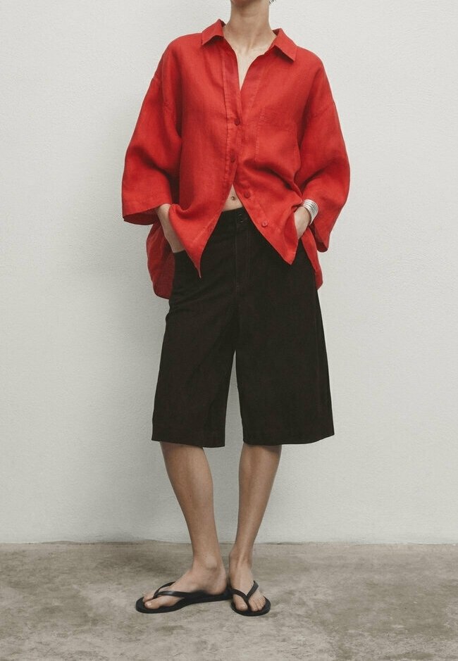 Chemise rouge en lin avec boutons, coupe décontractée, associée à un short marron foncé coupé au genou et des tongs noires. Design simple et décontracté.