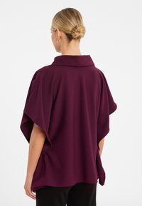 Burgunderfarbener, locker sitzender Oberteil mit weitem Kragen, kurzen Ärmeln und weicher Textur; fällt über den Körper mit seitlichen Schlitzen für Bewegungsfreiheit.