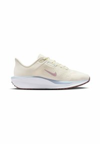 Beige athletic shoe with a textured mesh upper, pink Nike swoosh, and a cushioned white midsole. Outsole features red traction patterns.