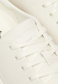 Sneaker bianche con tomaia in pelle liscia, punta rotonda, lacci piatti e cuciture tono su tono. Presenta una piccola etichetta con il marchio sulla linguetta.