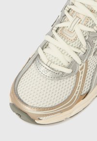 Sapatilha com cabedal em rede branca, detalhes em prata metálica e bege. Apresenta atacadores brancos planos e sola texturizada.