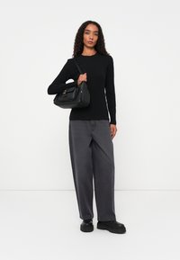 Top negro de manga larga de canalé, pantalones de pierna ancha grises, bolso negro con bolsillo delantero y zapatos negros de suela gruesa.