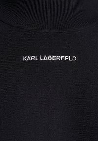 Tissu noir avec texte blanc brodé « KARL LAGERFELD » sous un col côtelé.