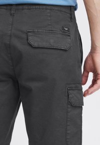 Pantaloni cargo gri închis cu o Textură netedă din bumbac. Caracteristicile includ buzunare laterale și un buzunar pătrat la spate cu o etichetă mică.