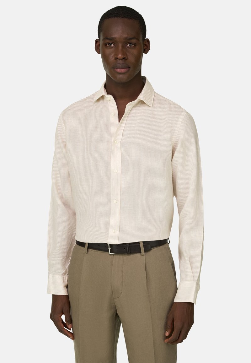 Homme portant une chemise à manches longues beige clair boutonnée et rentrée dans un pantalon kaki avec une ceinture noire, debout face à l'avant.