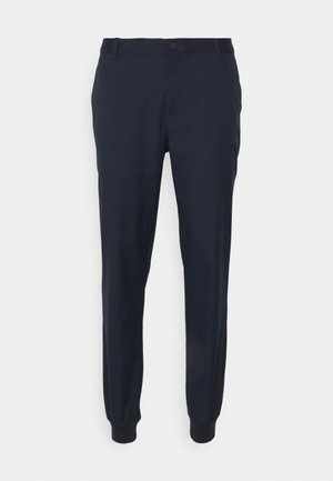 Joggers ajustados en azul marino con puños elásticos, cierre de botón y trabillas para cinturón. Fabricados con un tejido suave, presentan una textura lisa y líneas limpias.