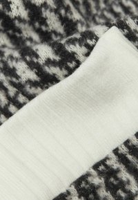 Stickad tyg med ett svartvitt mönster, kombinerat med ribbat vitt material. Texturerad yta med en mjuk, fluffig känsla.