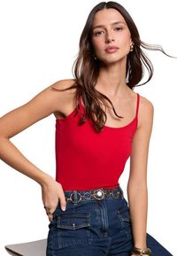 Débardeur rouge à fines bretelles, design ajusté, porté avec un jean en denim bleu taille haute agrémenté d'une ceinture circulaire dorée. Texture lisse.