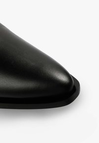Zapato de cuero negro con punta afilada, textura suave y suela plana. Presenta una silueta elegante y un diseño minimalista sin herrajes visibles.