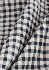 Sort-hvid ternet stof med en vævet tekstur. Mønsteret består af skiftevis firkanter i forskellige størrelser.