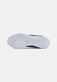 Zapatilla deportiva con parte superior morada, con un diseño texturizado. Suela de goma blanca con un patrón en la superficie para mayor agarre.