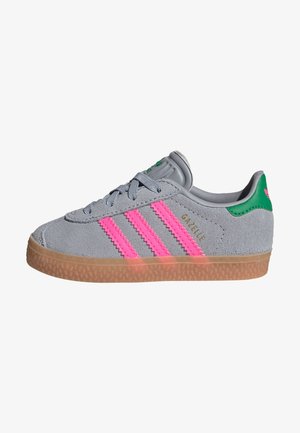 Gray suede sneaker with pink three-stripes, textured gum sole, green accents, and "Gazelle" logo on the side. Low-top design.