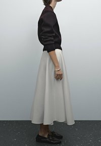 Dunkelburgunderfarbener Pullover, cremefarbene plissierte Rock und schwarze Schuhe. Der Pullover hat gerippte Bündchen; der Rock hat eine glatte, fließende Textur.