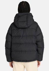 Zwarte pufferjack met een capuchon, gequilt ontwerp en een glanzende afwerking. De mouwen zijn iets oversized met een strakke pasvorm bij de manchetten.