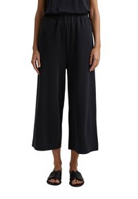 Pantalon noir à jambes larges avec taille élastique. Confectionné dans un tissu lisse et léger. Caractérisé par une coupe ample et une longueur raccourcie.