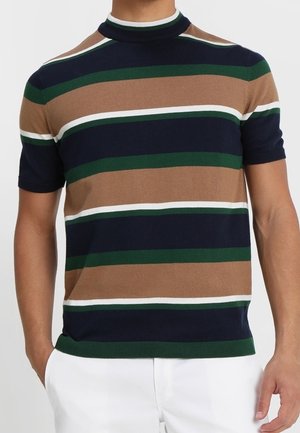 Homme portant un pull en maille à manches courtes avec des rayures horizontales bleu marine, marron, vert et blanc, associé à un pantalon blanc.