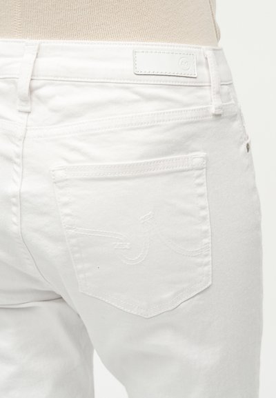 Κοντινό πλάνο της πίσω τσέπης λευκού τζιν με διακριτική ραφή και δερμάτινο ταμπελάκι με το λογότυπο στη μέση της ζώνης.