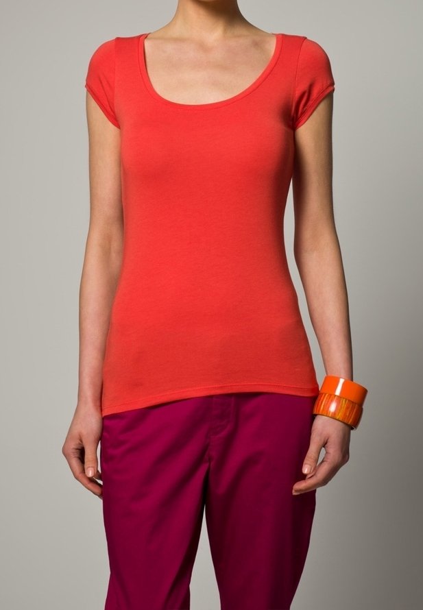 Camiseta de algodón roja con mangas cortas tipo capucha y escote en forma de U, combinada con pantalones rosas vibrantes y una pulsera ancha naranja.