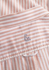 Camicia a righe con strisce rosa chiaro e bianche, con un dettaglio ampersand ricamato di colore blu scuro e un colletto strutturato.