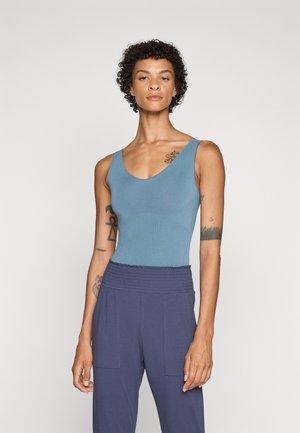 Sleeveless blue bodysuit with a deep V-neck, smooth texture, paired with high-waisted navy trousers featuring a gathered waistband and side pockets.