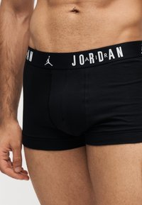 Torse masculin portant un boxer Jordan noir avec une ceinture à logo et un anneau de nombril argenté visible.