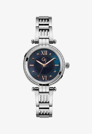 Sudraba nerūsējošā tērauda pulkstenis ar apaļu zilu ciparnīcu, zelta akcentiem, romiešu cipariem 12 un 6, kā arī teksturētu metāla rokassprādzi.