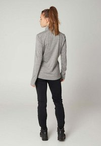 Graues Langarmshirt mit hohem Kragen, kombiniert mit schwarzen Hosen und robusten schwarzen Stiefeln, von hinten vor einem schlichten Hintergrund gezeigt.