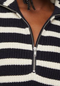 Sweter w paski w kolorze granatowym i kremowym, dzianinowy, z zamkiem błyskawicznym przy szyi, charakteryzujący się teksturowanym materiałem i solidnym metalowym zamkiem.