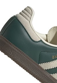 Grön lädersneaker med mockadetaljer, räfflad häl och texturerad gummisula. Har guldfärgad märkning och kontrasterande beige ränder.