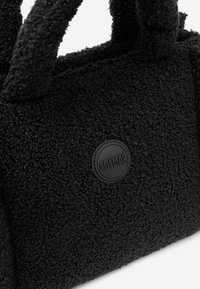 Melnas strukturētas auduma soma ar īsām rokturiem, kurā ir aplis melns Colmar logos. Virsma ir pūkaina ar mīkstu, taustāmu izskatu.