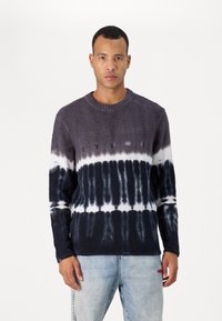 Pull en tricot gris foncé avec un motif tie-dye arborant des accents blancs et bleu marine. Encolure ronde et manches longues, texture douce, coupe décontractée.