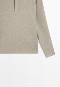 Beige long-sleeve knit sweater with a ribbed texture and a partial front placket detail against a white background.