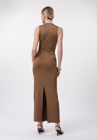 Brun, figurnära maxiklänning med hög hals och en slits bak. Tillverkad av slätt tyg, har den en elegant silhuett och minimal detaljering.