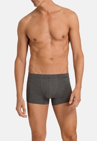 Tumma harmaat bokserit, jotka on valmistettu pehmeästä kankaasta, keski-ylösuunnassa olevalla digitaalisella muotoilulla, muotoon ommellulla taskulla ja kontrastivärisillä saumoilla. Ei näkyviä logoja.