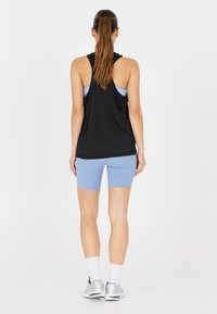 Mustaväriinen hihaton paita, jossa on rento malli, yhdistettynä vaaleansinisiiin pyöräilyshortseihin. Hopeiset urheilukengät ja valkoiset sukat näkyvissä, kokonaisuudessa minimalistinen muotoilu.