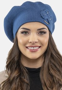 Beret tricotat albastru cu suprafață texturată, prezentând un accent floral tridimensional și mici embellishments decorative.