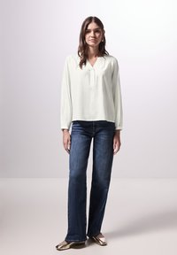 Lichtgroene blouse met een V-hals en knoopsluiting, gecombineerd met donkerblauwe wijde jeans en metallic gouden flats. Gladde textuur, casual stijl.